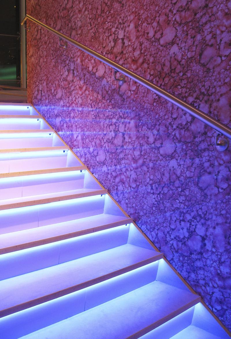 Bei eine Voutenbeleuchtung einer Treppe für Stufen, wurden spezielle Lichtrofile mit kaltweißen LED-Stripes eingesetzt. Der Handlauf mit integrierten einfarbigen LED-Leuchtmittel iilluminiert die untere Wand. Durch versteckte Bewegungsmelder entfällt eine Lichtschaltung.