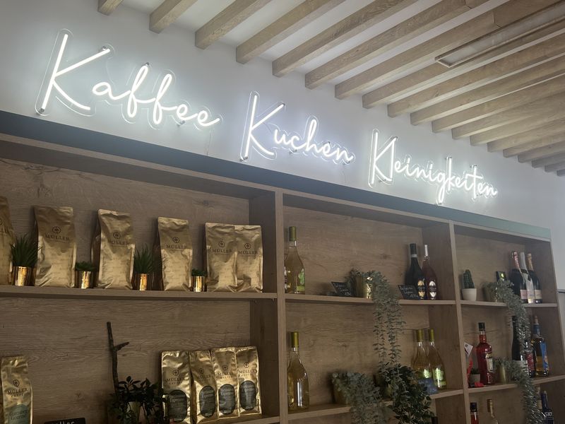 LED-Neon Schriftzug im Kaffee Innenwerbung mit LED-Neon zum Blickfang im Kaffee. Die weiß leuchtender Leucht-Handschrift ist eine Lichtwerbung, wo das Angebot „Kaffee, Kuchen, Kleinigkeiten“ zu sehen ist. Es schafft eine einladende, warme Atmosphäre im Gastraum.