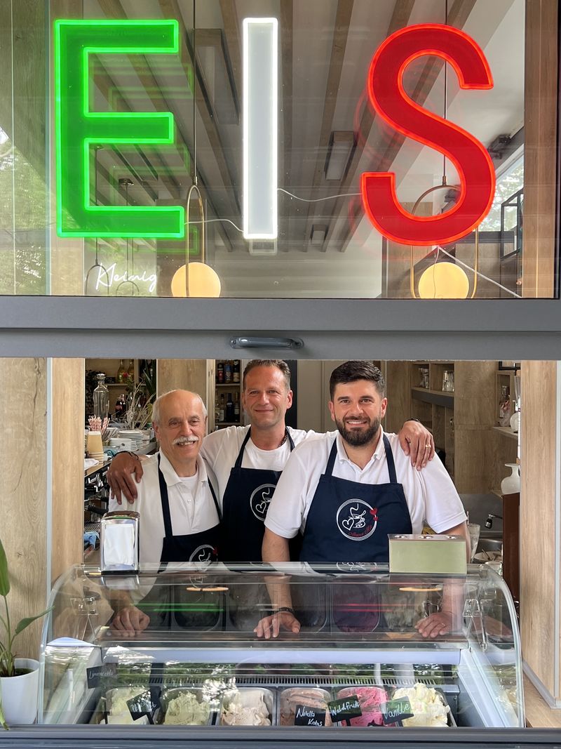 Moderne LED-Neon Leuchtschrift „EIS“ über der Eistheke, deren drei große Buchstaben jeweils in einer eigenen Farbe entlang als Konturbeleuchtung sind. Die umlaufende LED-Neon Beleuchtung erzeugt einen klaren, intensiven Lichtschein und macht das Angebot bereits von außen durch das Fenster sichtbar.