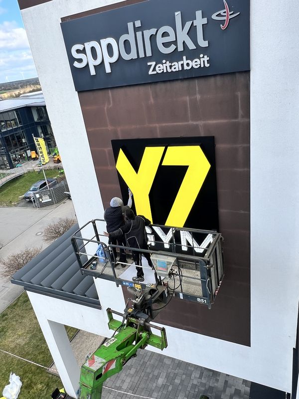 Fachgerechte Montage einer XXL-Außenwerbeanlage. Das markante Y7-GYM Logo aus gelben LED-Profilbuchstaben sorgt für maximale Fernwirkung und Sichtbarkeit an der Außenfassade.