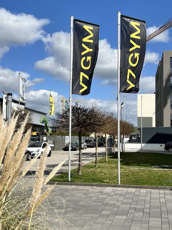 Großformatige Hissflaggen für das Y7 GYM sorgen schon von weitem für Aufmerksamkeit. Die schwarz-gelben Fahnen nutzen die Windbewegung für maximale Sichtbarkeit. Die gelb-schwarzen Flaggensysteme des Y7 GYM nutzen die natürliche Bewegung des Windes, um Blicke einzufangen.