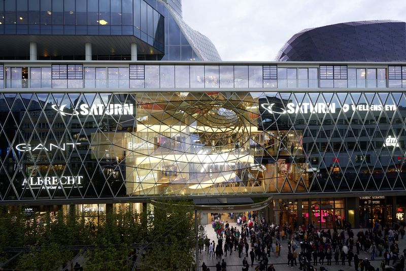 Dieses Foto zeigt die Glasfassade des MyZeil Shopping-Centers bei Dämmerung. Man erkennt deutlich die Integration der Lichtwerbungen von Innen nach Außen leuchtend in die komplexe Geometrie des Gebäudes, was für maximale Sichtbarkeit und Markenwirkung sorgt.