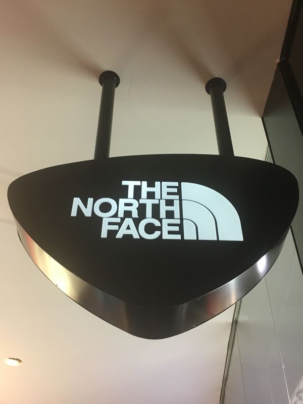Für den Store von The North Face im MyZeil haben wir dieses elegante Nasenschild realisiert. Das Logo wurde präzise aus der schwarzen Front gefräst und mit einer hochwertigen LED-Hinterleuchtung versehen, die für ein klares, blendfreies Lichtbild sorgt. Die Montage erfolgte sicher an der Deckenkonstruktion mittels dezenter schwarzer Halterungen.