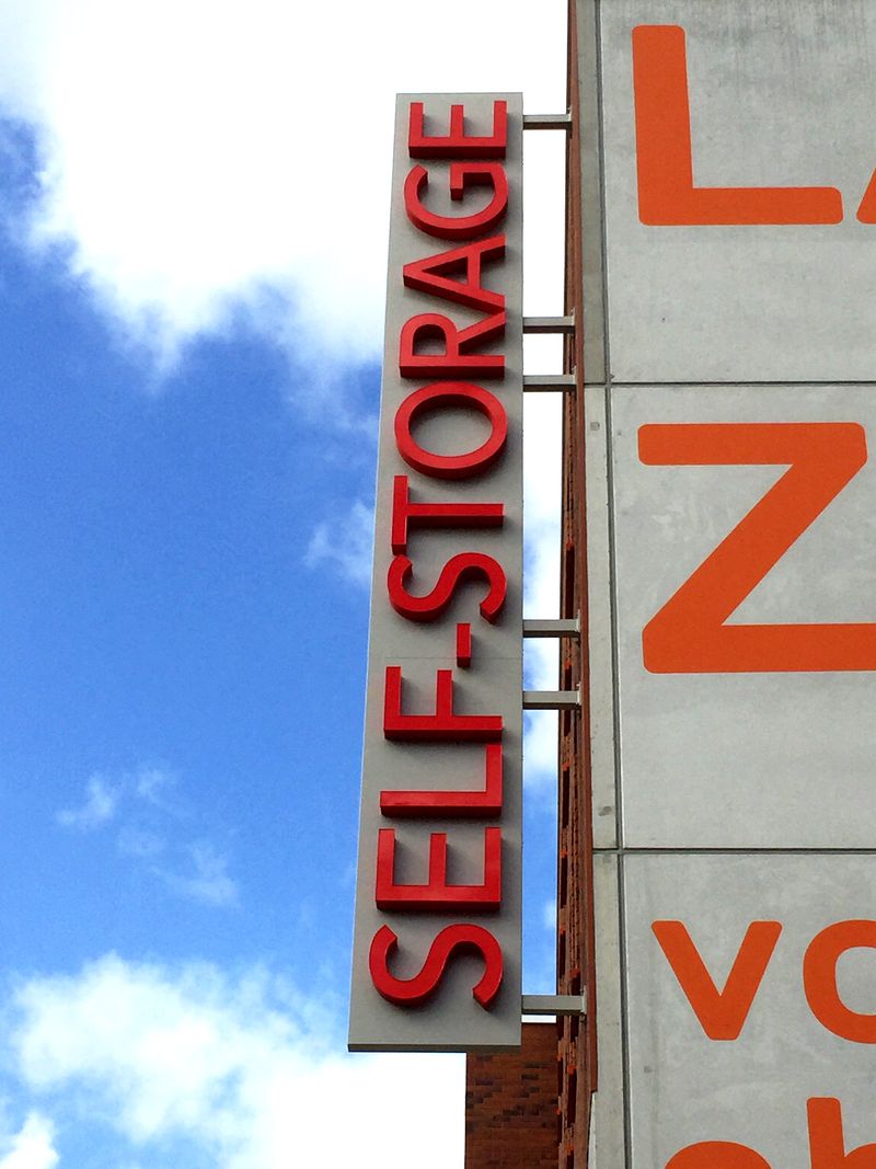 Vertikales Nasenschild (Ausleger) mit roten Profilbuchstaben „SELF-STORAGE“ an einer Gebäudefassade. Fachgerechte Befestigung mittels massiver Wandhalterungen und optimale Höhe für eine gute Sichtbarkeit aus jedem Blickwinkel.