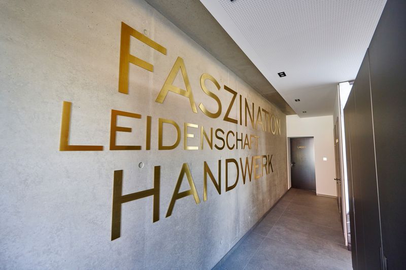 Eine Beschilderung an der Flurwand im Innenbereich des Weinguts, die durch eine hochwertige veredelte Metall-Schrift montiert wurde. Die  Innenbeschilderung wurde durch Großformatige Metall-Buchstaben in Gold-Optik auf Sichtbeton befestigt.