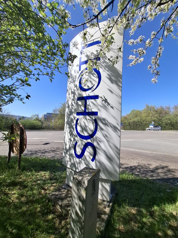  Der Werbepylon Schott, der in der Dämmerung strahlt und die Aufmerksamkeit aller Passanten und Autofahrer auf sich zieht, hat ein klares, modernes Design, das das Firmenlogo präsentiert. Das Logo ist durchleuchtet und leuchtet in blauer Lichtfarbe, so das der Pylon in der Abenddämmerung besonders gut zur Geltung kommen.