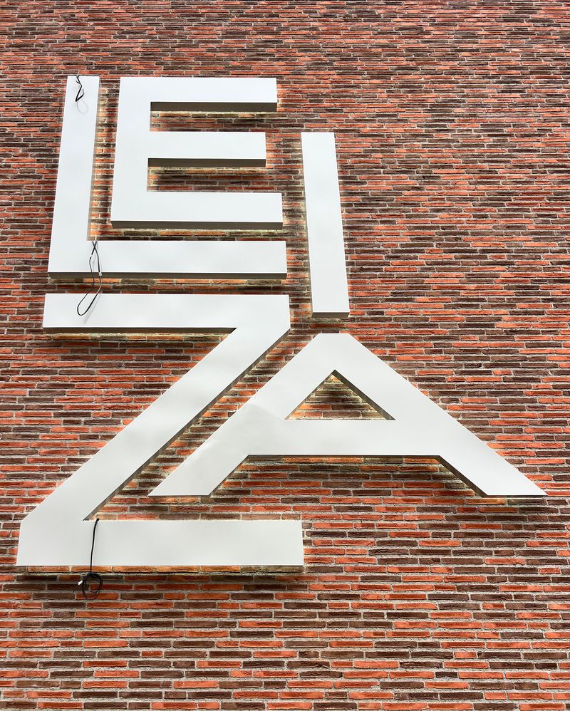 Fertige Montage der dreidimensionalen Profilbuchstaben, die das Firmenlogo Leiza zeigen. Ein gleichmäßiger Lichtschatten auch Halo-Beleuchtung oder Corona genannt, entsteht durch eine Rückbleuchtung mit Abstandshalterung. Eine Lichtwerbeanlage mit gleichmäßige und energieeffiziente Ausleuchtung als Außenwerbung.