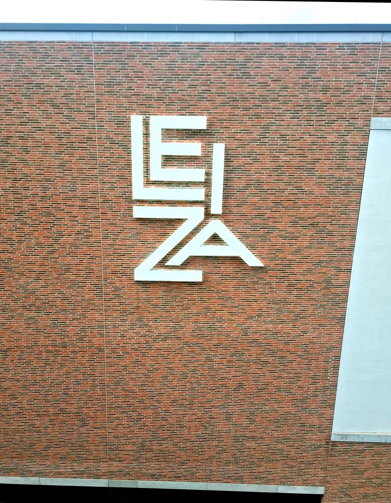 Weiße Aluminium-Profilbuchstaben des LEIZA-Logos mit indirekter LED-Rückbeleuchtung (Halo-Beleuchtung) hinter den Profilbuchstaben direkt an einer modernen Klinkerfassade montiert. Die hochwertige Fassadenwerbung sorgt tagsüber für eine elegante Optik und nachts für eine gleichmäßige Schattenbeleuchtung.